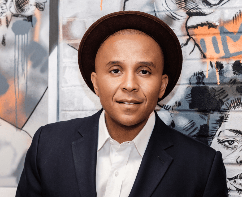 Headshot of Color of Change President Rashad Robinson standing in front of a color wall.