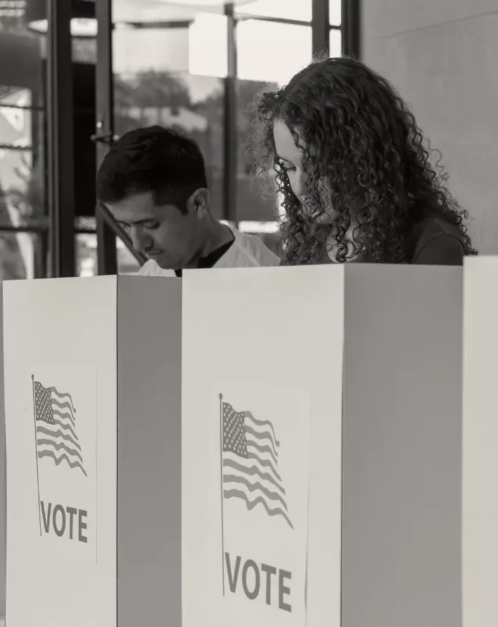 Two people vote behind privacy folders.